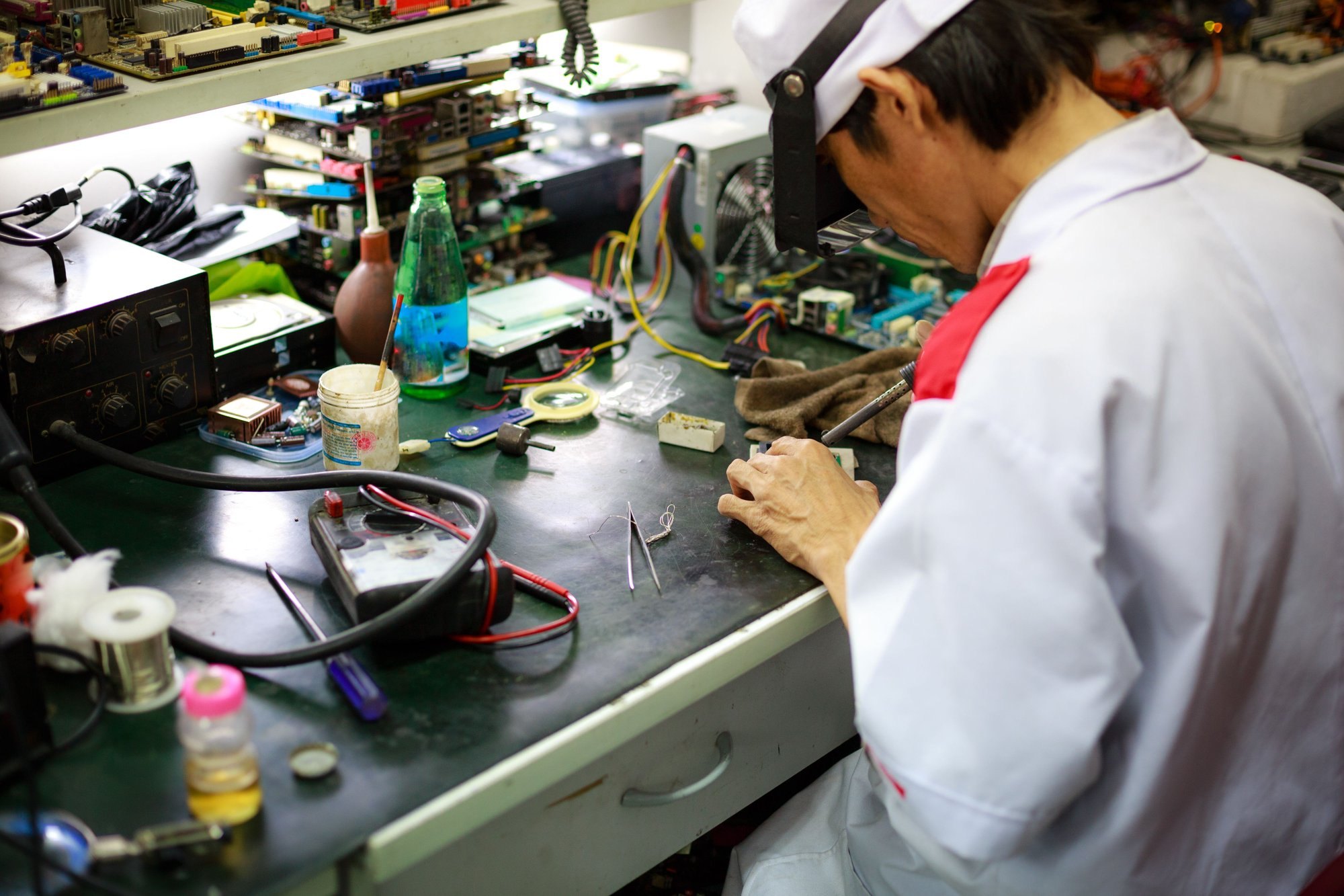 Technician working at an electronics test and repair bench with a multimeter and power supply.