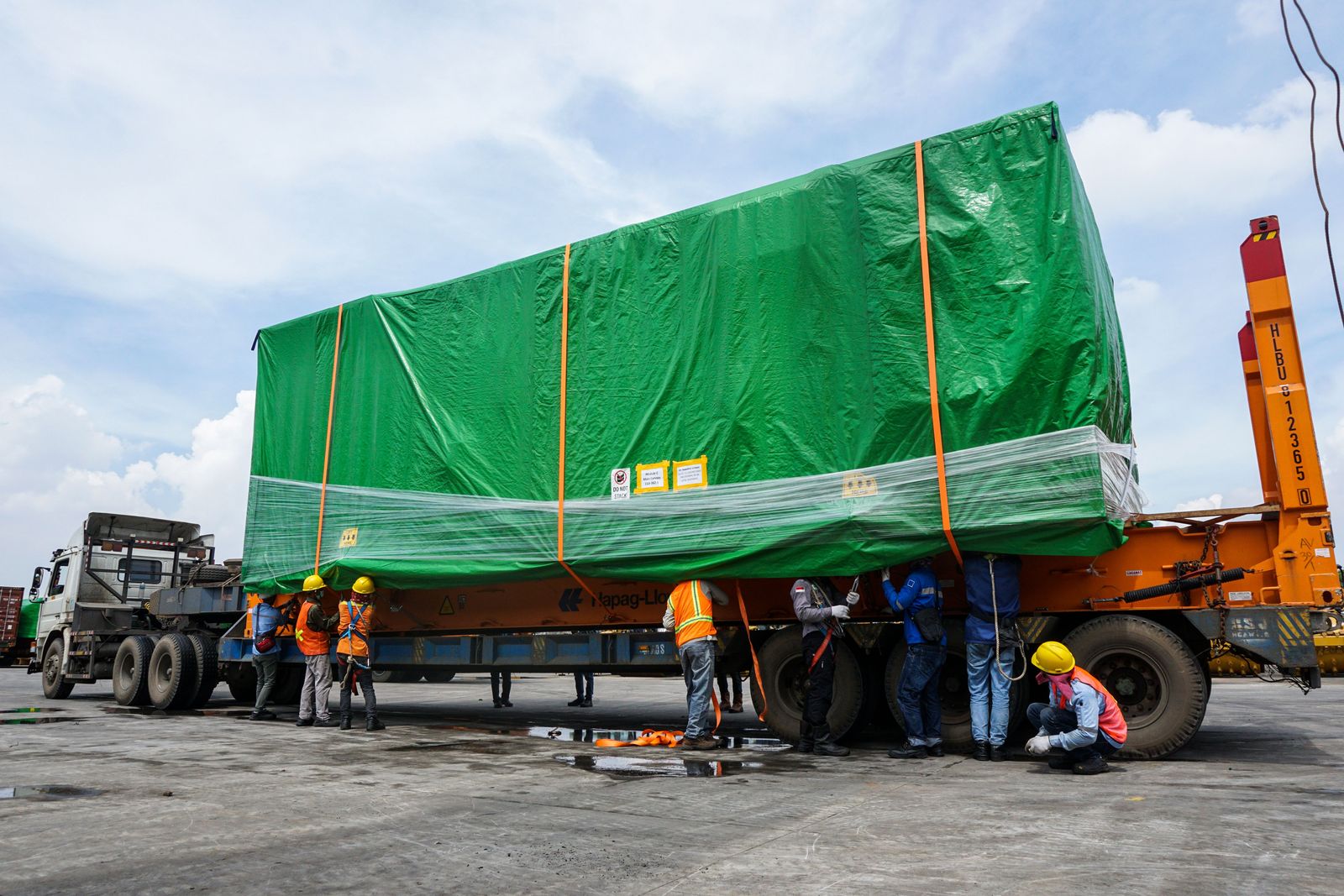 Crew securing a large covered machine load on a heavy trailer.