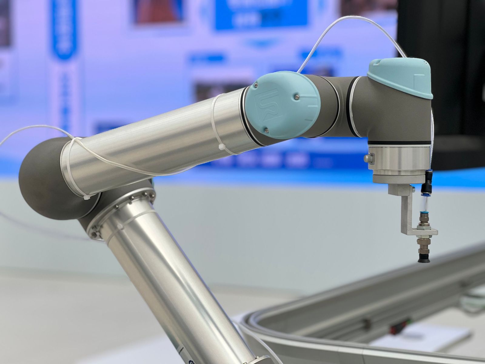 Collaborative robot arm with a suction tool over a conveyor.