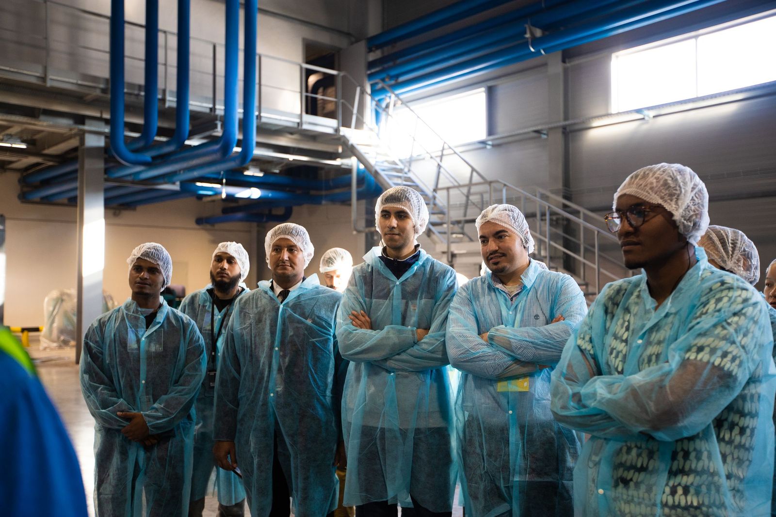 Leadership group in protective gowns touring a production hall.