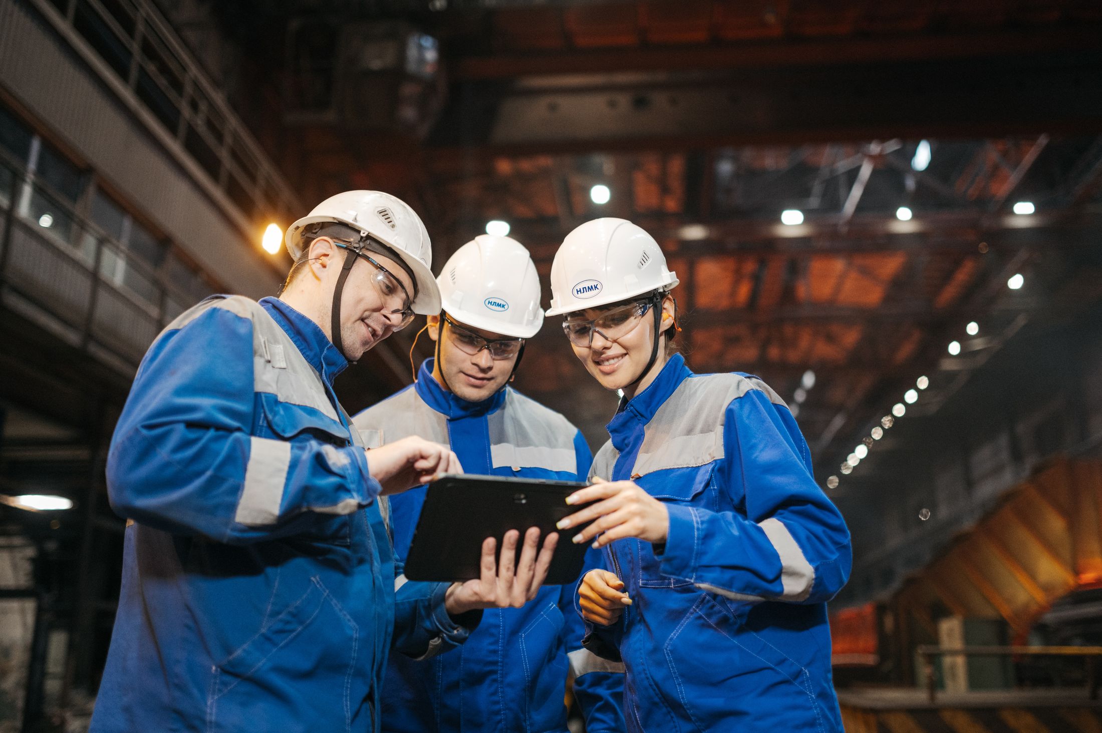 Three engineers reviewing production data on a tablet on the shop floor.