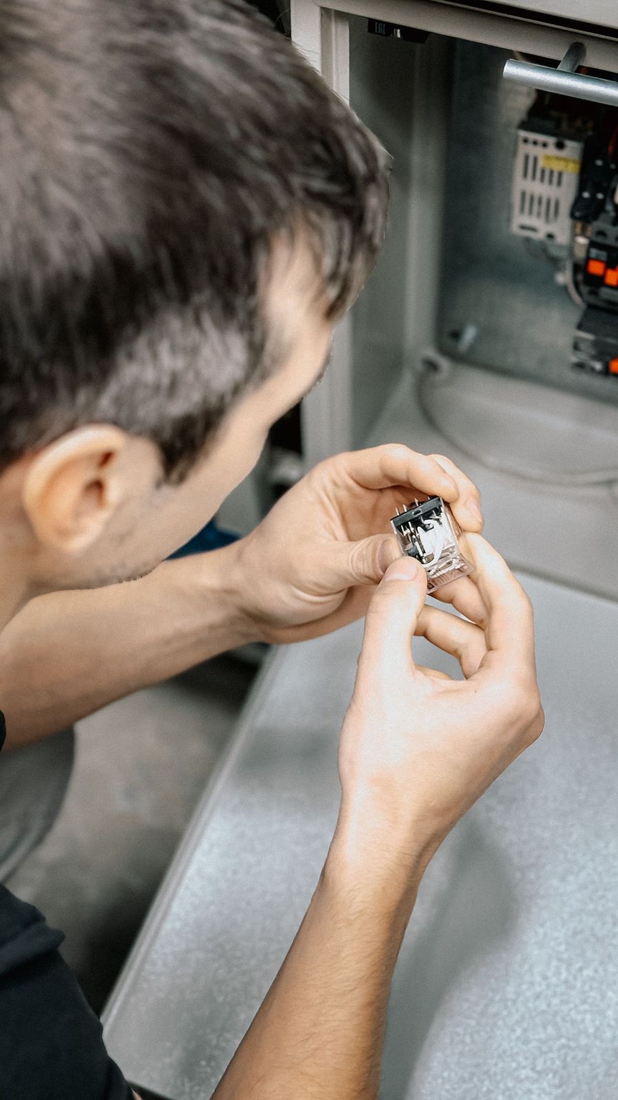 Technician inspecting a component inside a machine control panel.