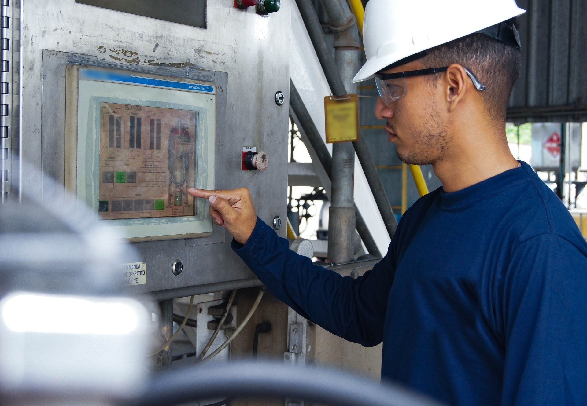 Engineer in a hard hat checking process data on a machine touch panel.