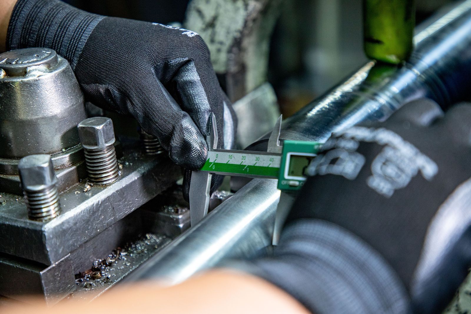 Gloved hands measuring a part on a machine with a caliper.