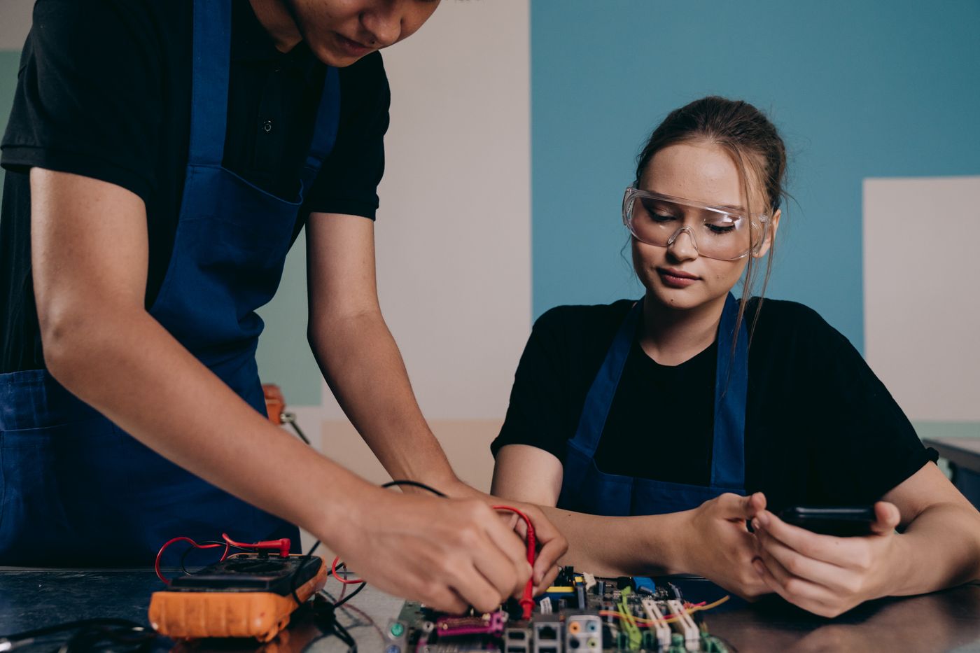 Two colleagues checking an electronic circuit with a multimeter.