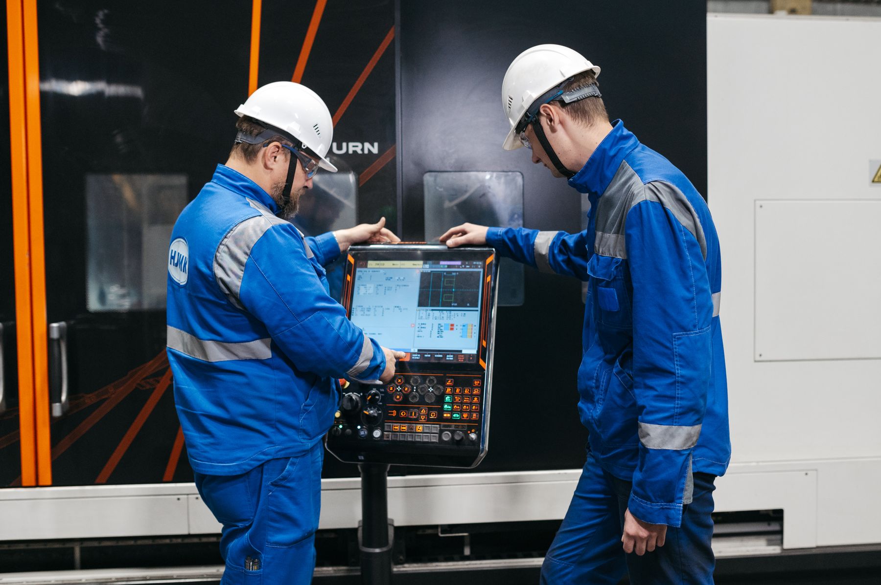 Two engineers reviewing machine data at a CNC control panel.